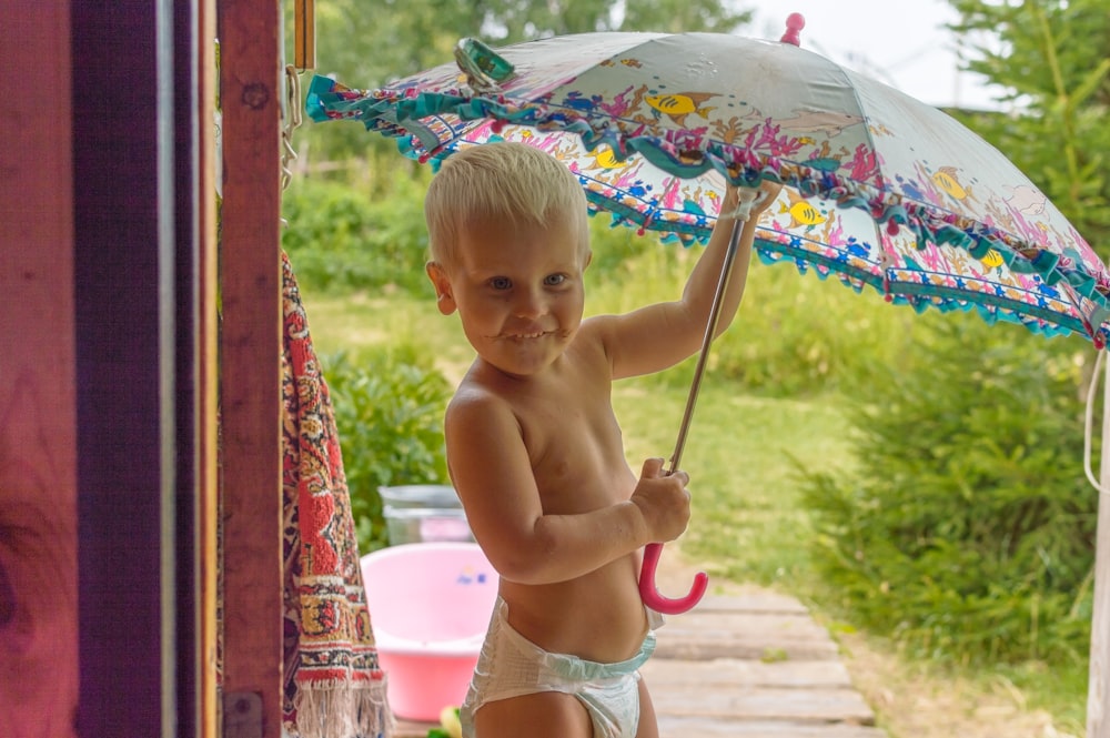 topless baby holding umbrella while sitting on concrete floor during daytime