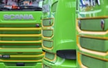 Close-up view of the front grills of two bright green trucks with yellow trim. The trucks have the brand name prominently displayed in large letters above the grills. The design features bold lines and a glossy finish.