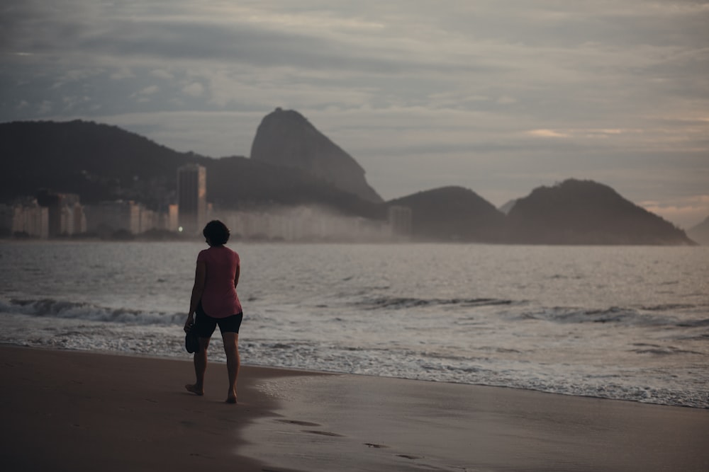 woman in red jacket standing on beach during daytime