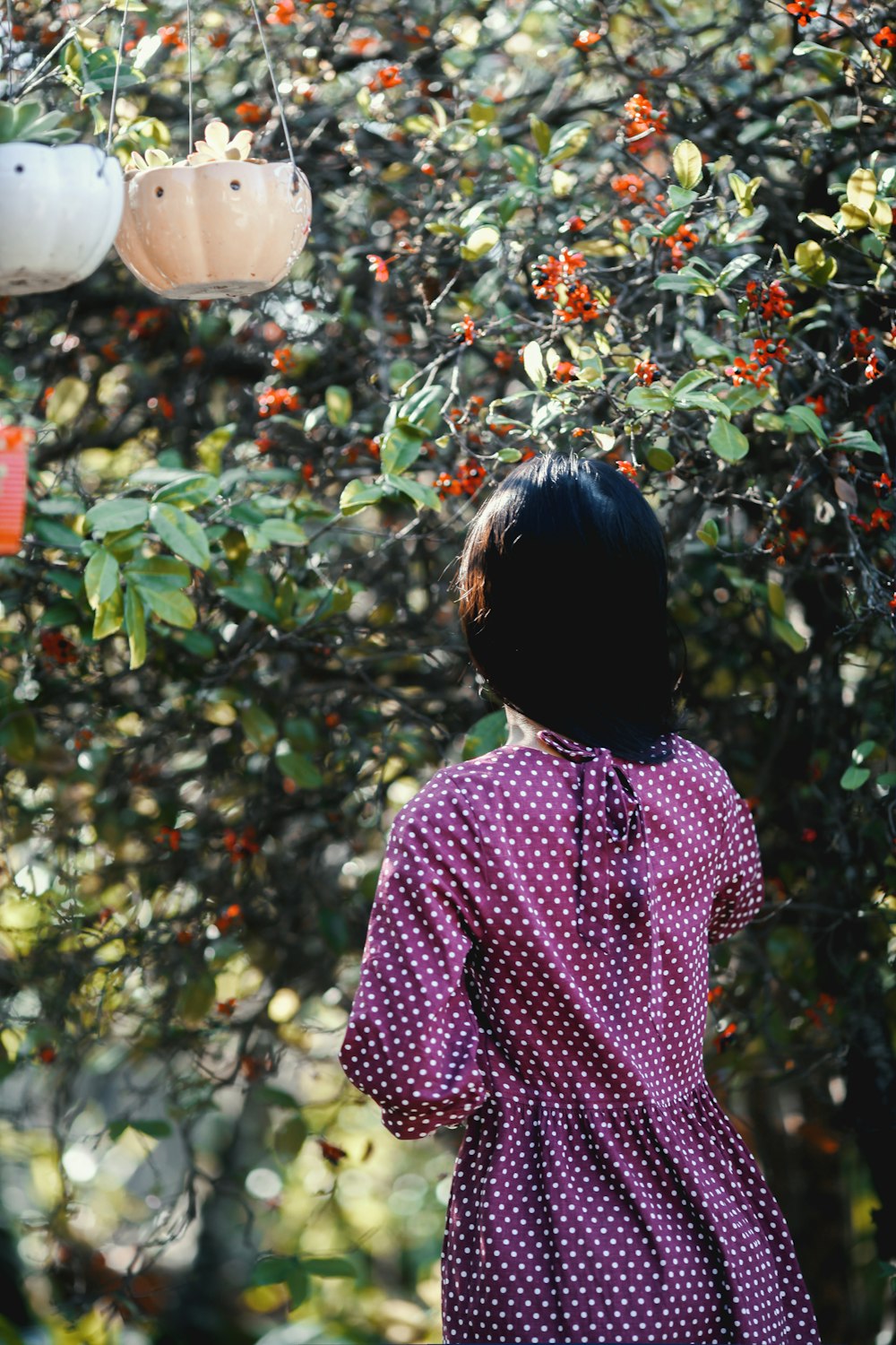 woman in purple and white polka dot shirt standing near green plants during daytime