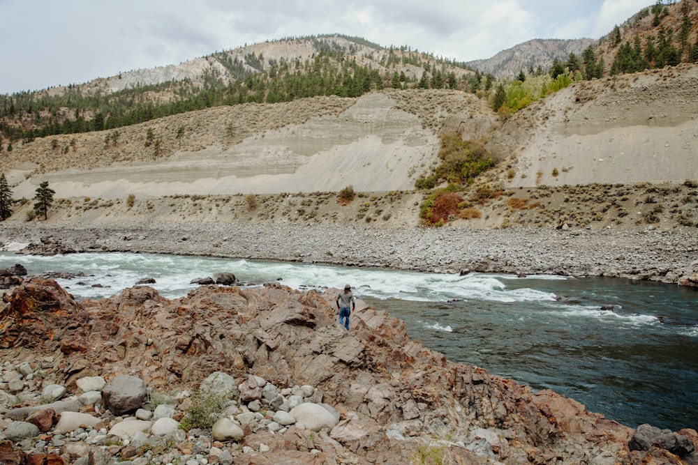 person in blue shirt and blue denim jeans walking on rocky shore during daytime