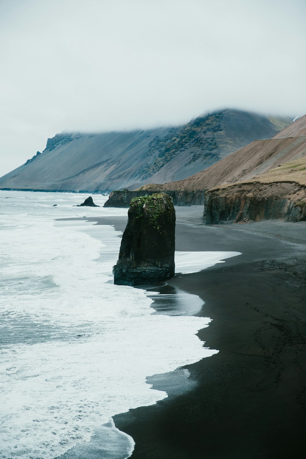 person standing on seashore near brown and green mountain during daytime