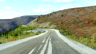 A serene mountain road winding through green hills under a clear blue sky.