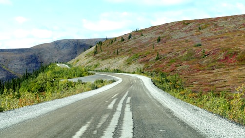 A winding mountain road surrounded by lush greenery under a bright blue sky.