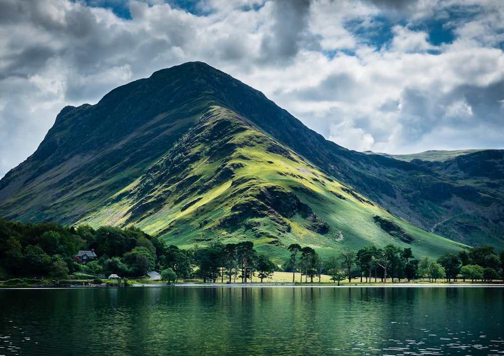 green mountain beside body of water under cloudy sky during daytime