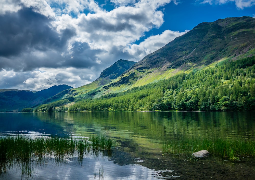 green mountains beside body of water under blue and white sunny cloudy sky during daytime