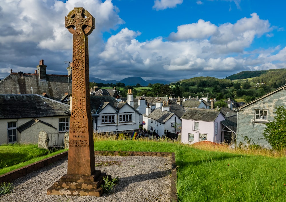 brown cross on green grass field near houses under blue and white cloudy sky during daytime