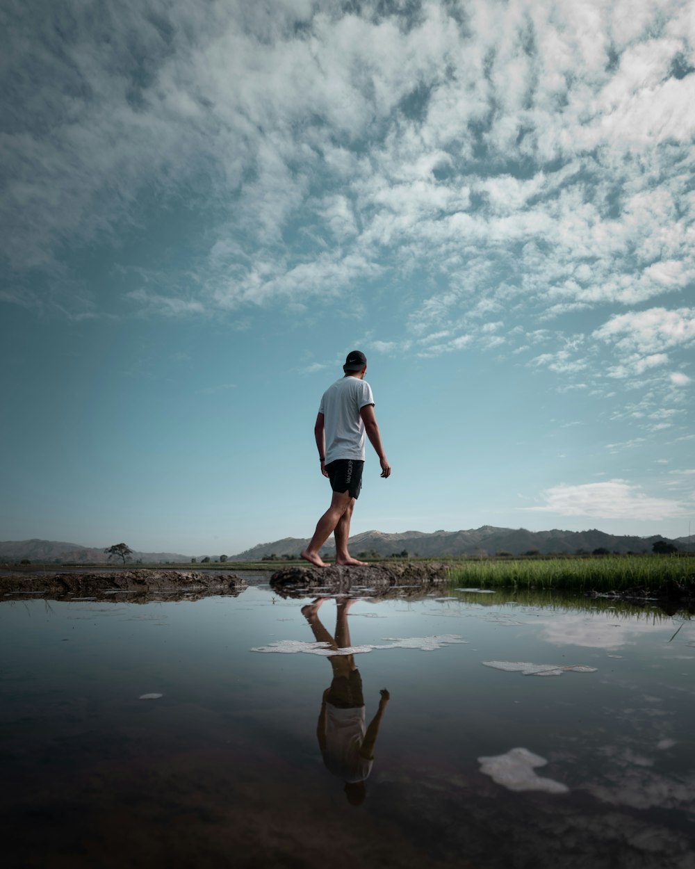 man in white t-shirt and blue shorts standing on brown tree log on lake during