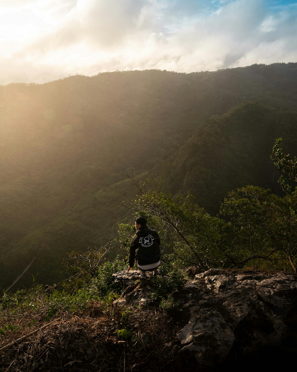 man in black jacket sitting on rock mountain during daytime