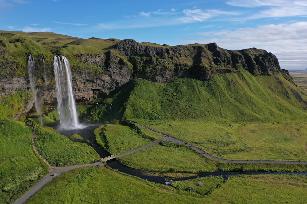 waterfalls on green grass covered hill under blue sky during daytime