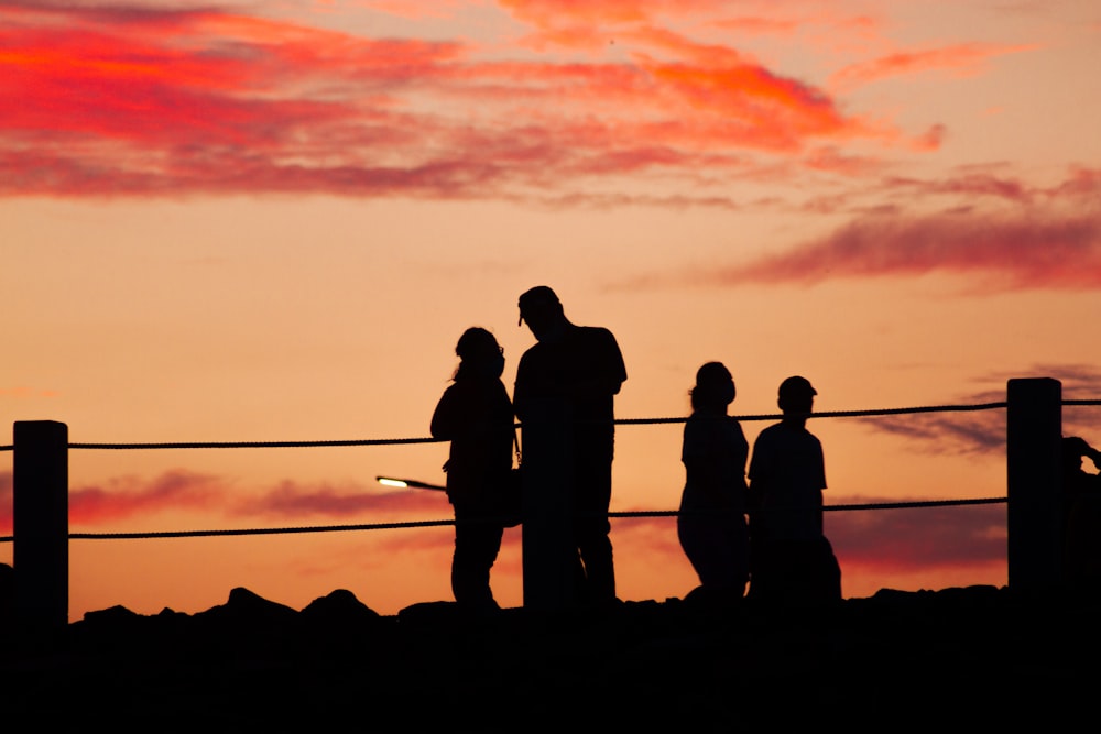 silhouette of people standing on rock during sunset