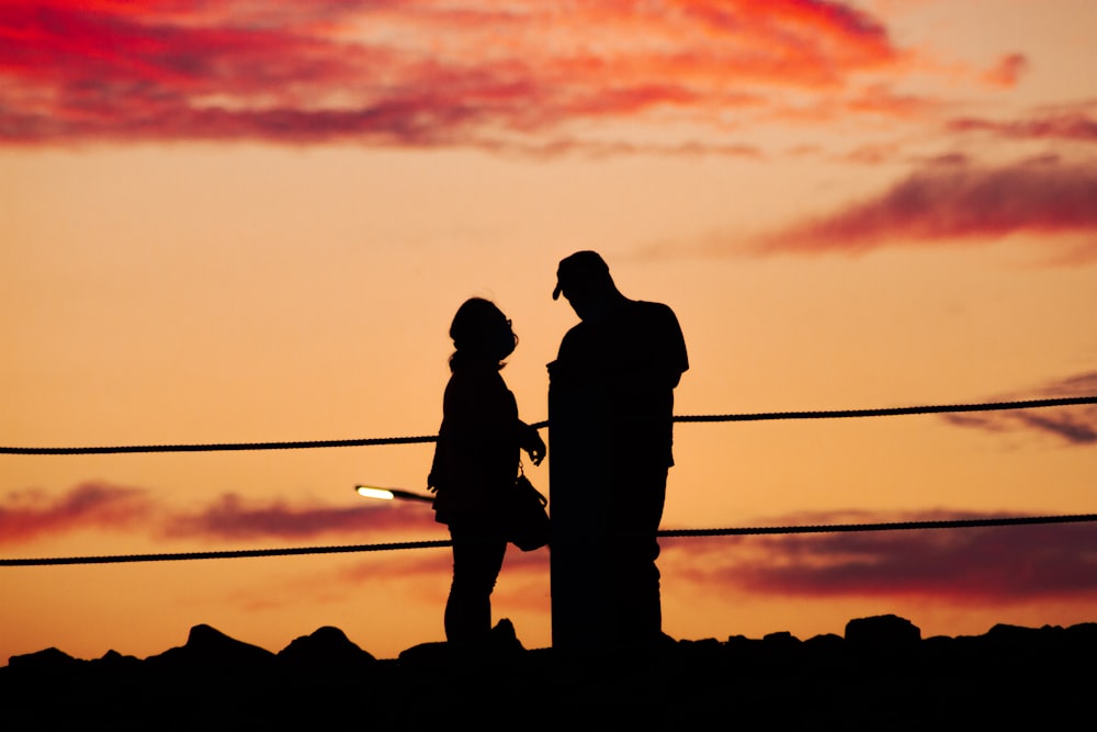 silhouette of 2 men standing on rock during sunset