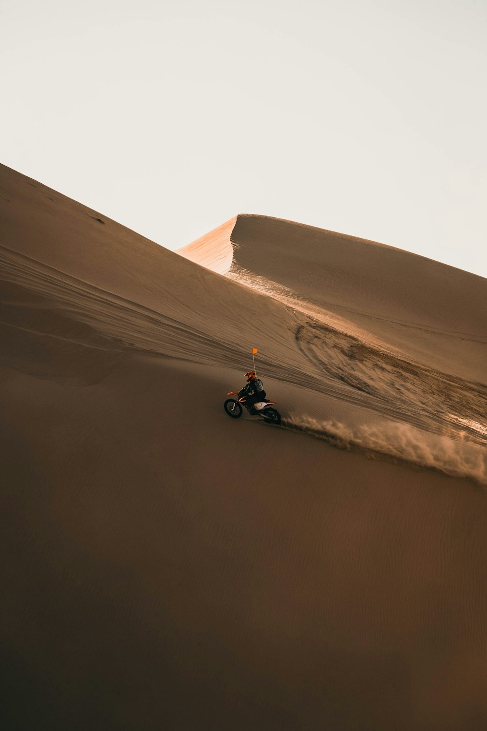 Mann in schwarzer Jacke fährt tagsüber schwarzes Motorrad auf braunem Sand