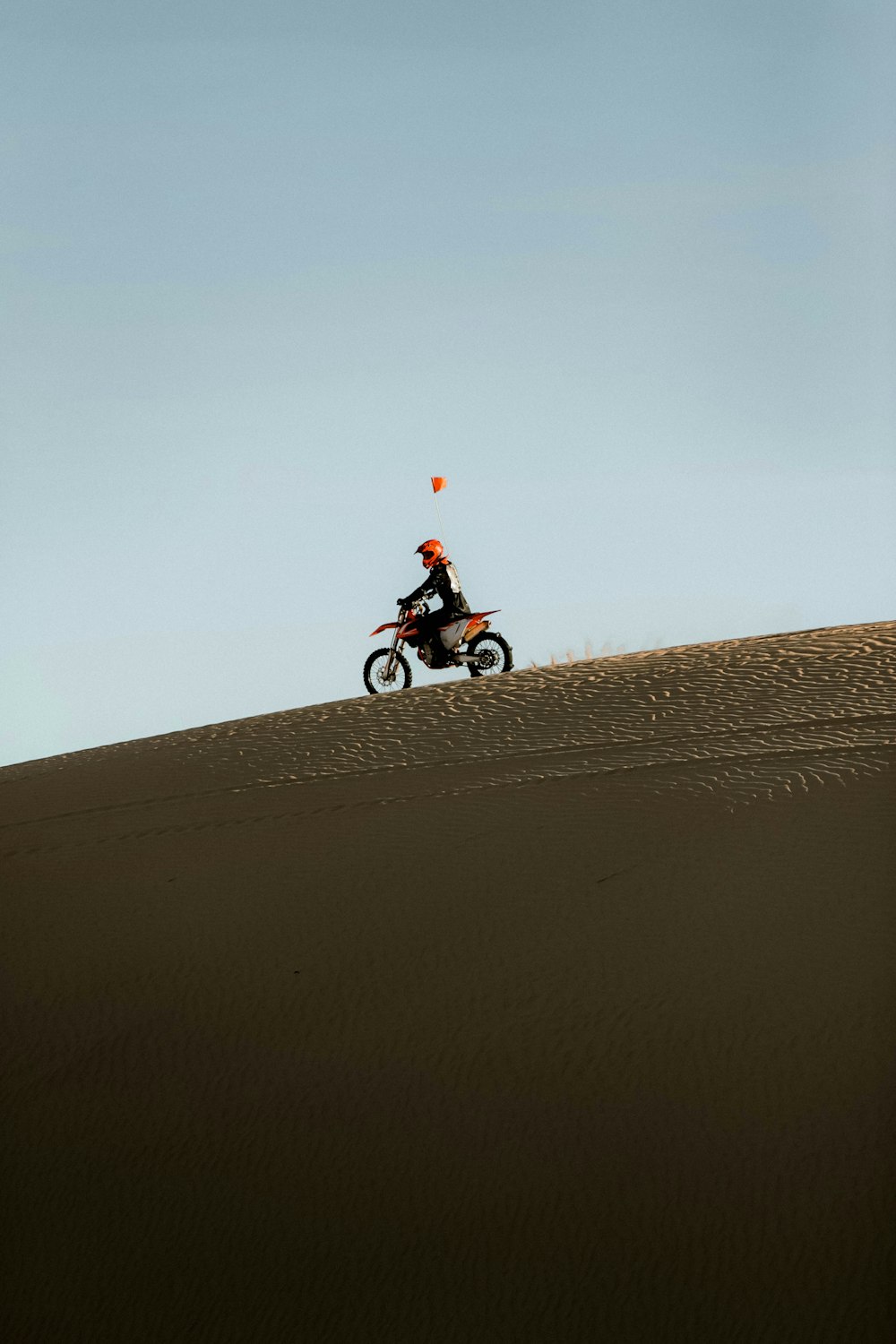 昼間、茶色の砂浜でバイクに乗る赤いシャツの男