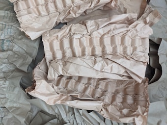 Crumpled brown paper with a textured, ribbed pattern is scattered across the surface. The paper appears to be used for packaging or cushioning, providing a layered and uneven appearance.