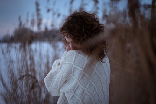 woman in white knit scarf standing on snow covered field during daytime