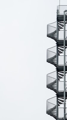 A series of metal spiral staircases ascend vertically with a minimalist background, highlighting the industrial design of the staircases.