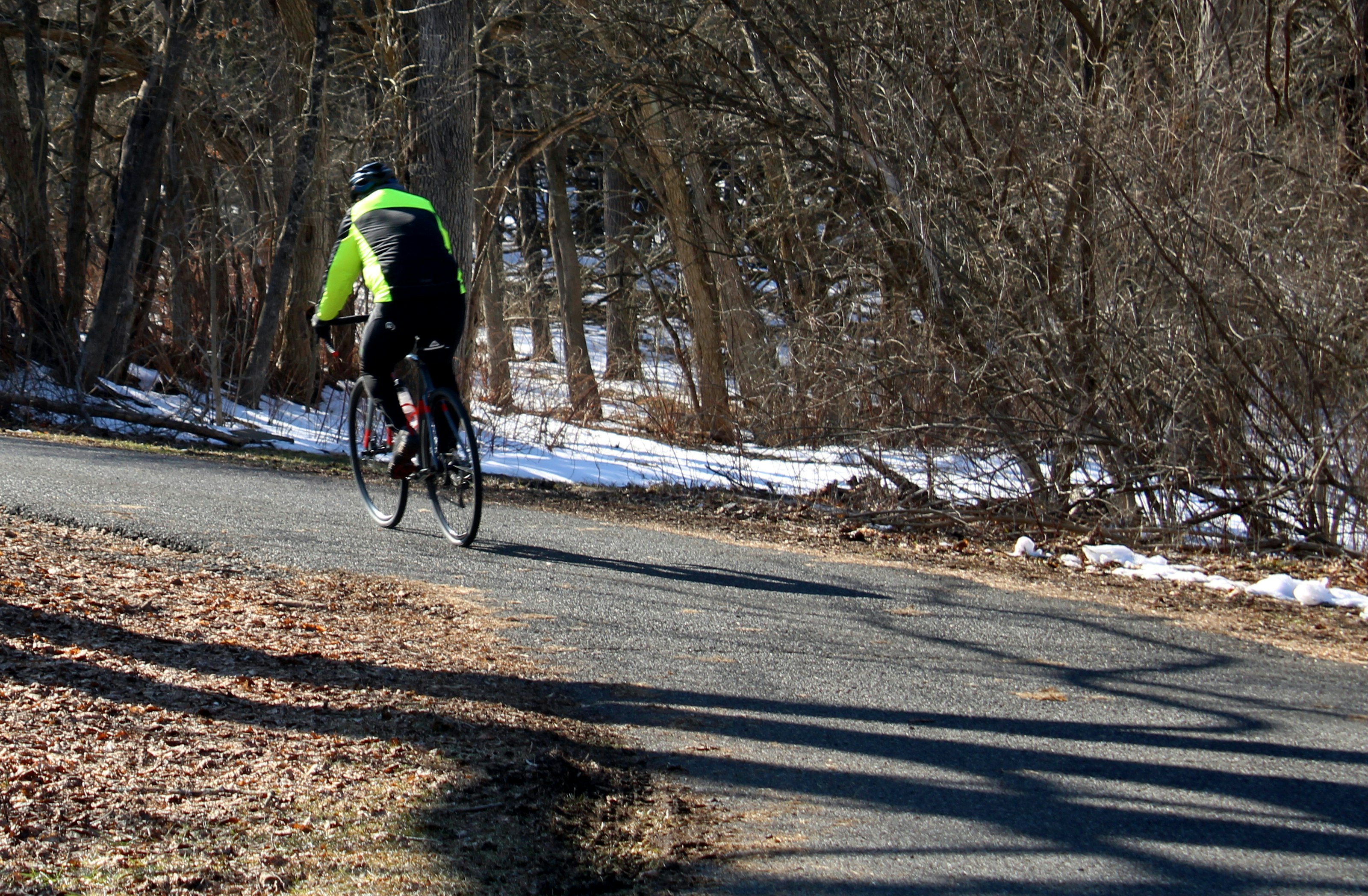 A speeding bicyclist, his legs pumping furiously as he rounds a paved trail curve March 3, 2021, at Evansburg State Park in Collegeville PA, is suited for the day's warmer-then-usual spring-like weather.