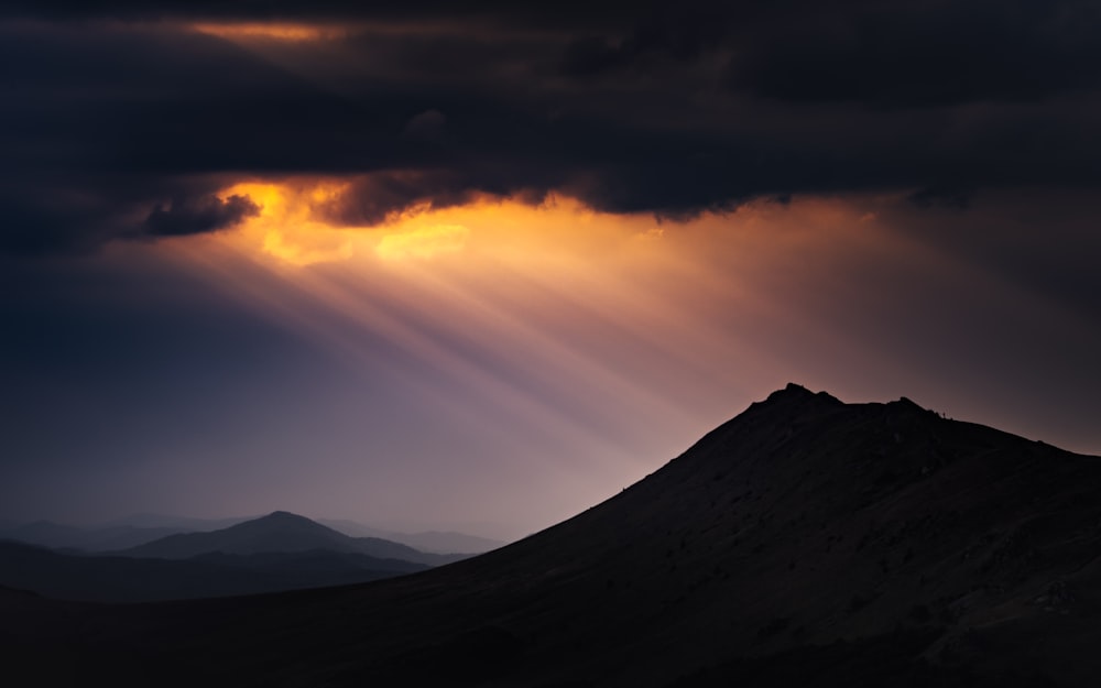 silhouette of mountains under cloudy sky during sunset