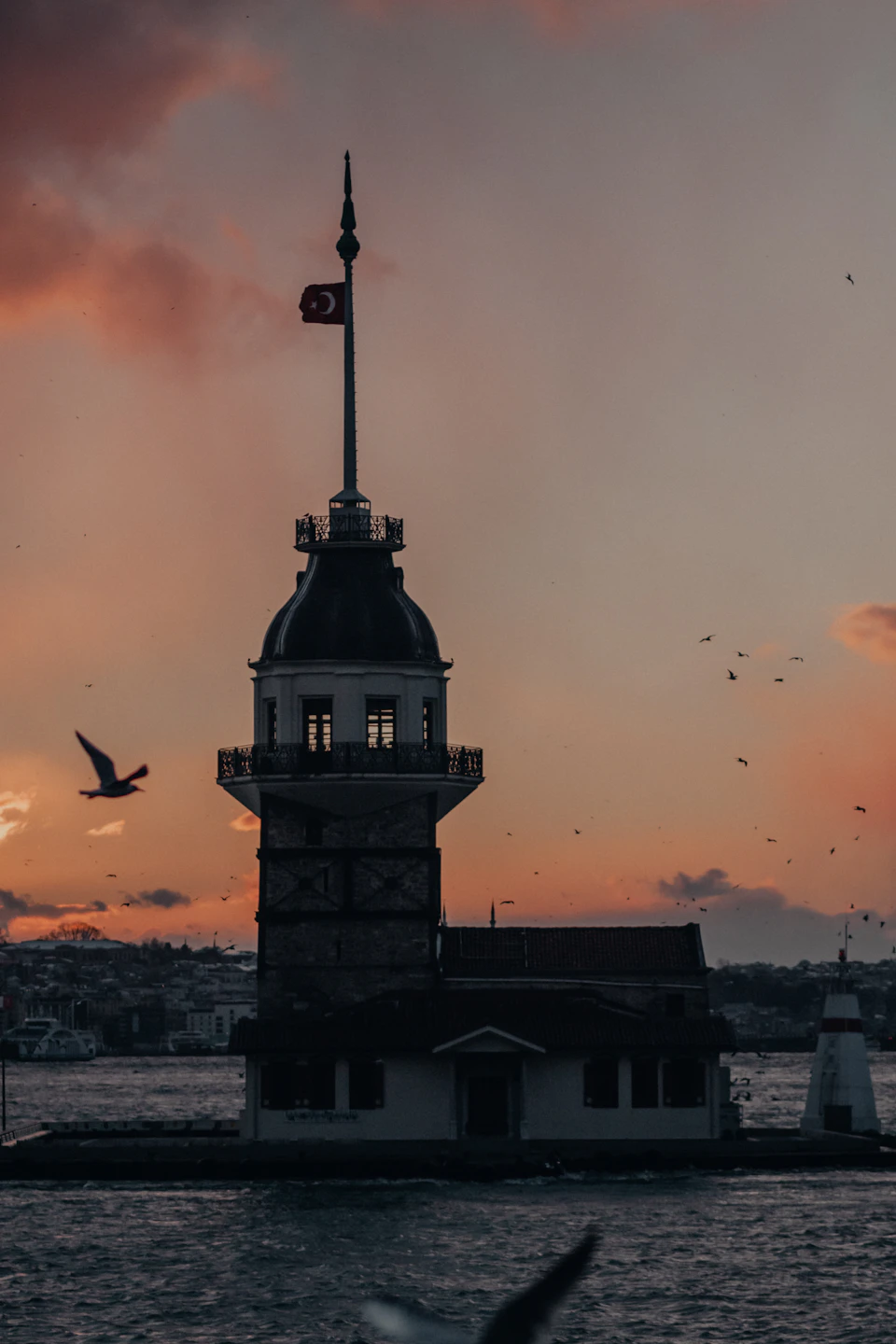 Bosphorus Lighthouse stands tall with a white roof and black dome against orange sky