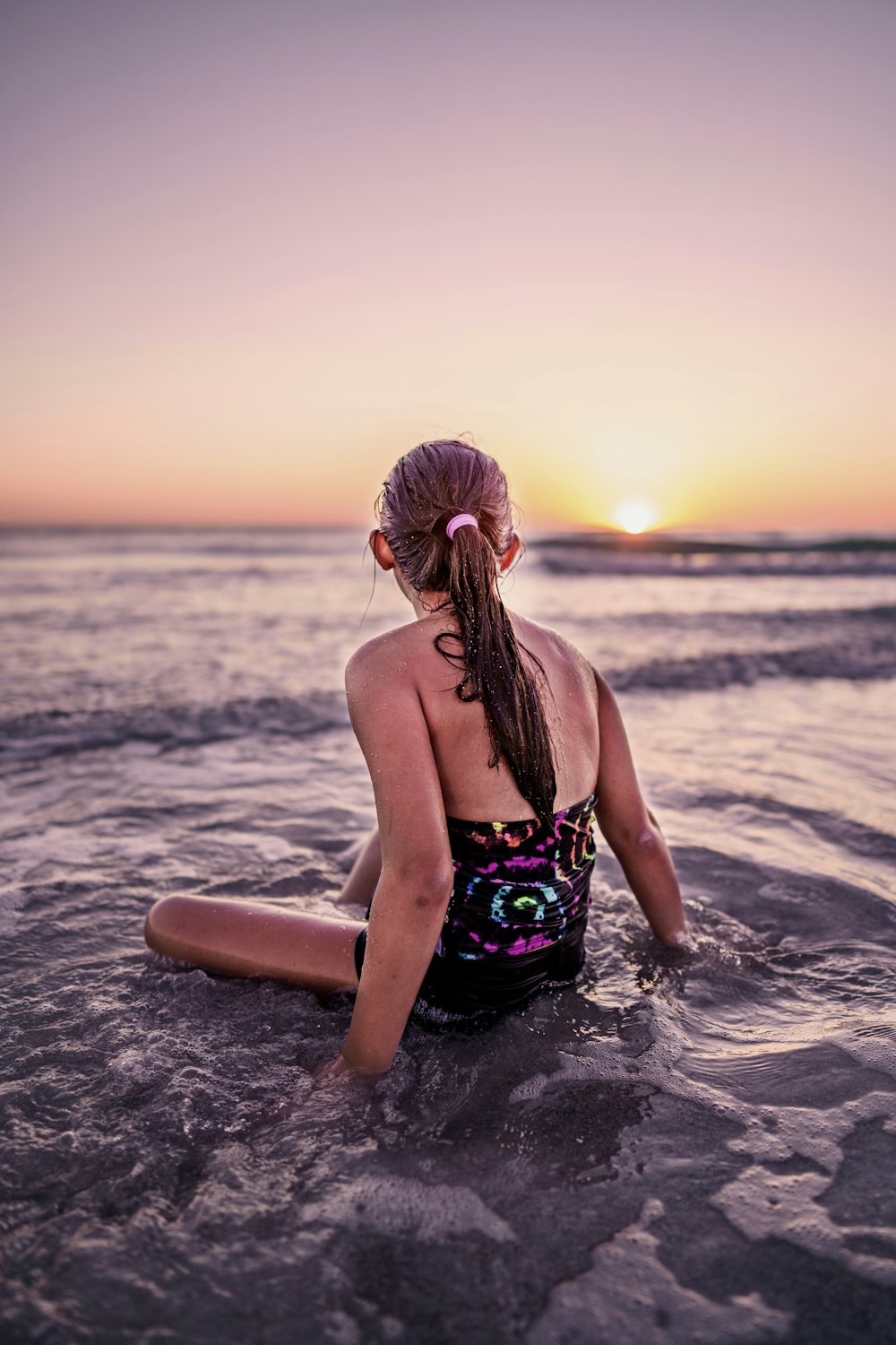 donna in bikini floreale verde e nero seduta sulla spiaggia durante il tramonto