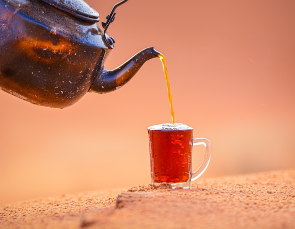 A rustic teapot pouring fragrant tea into a delicate porcelain cup.