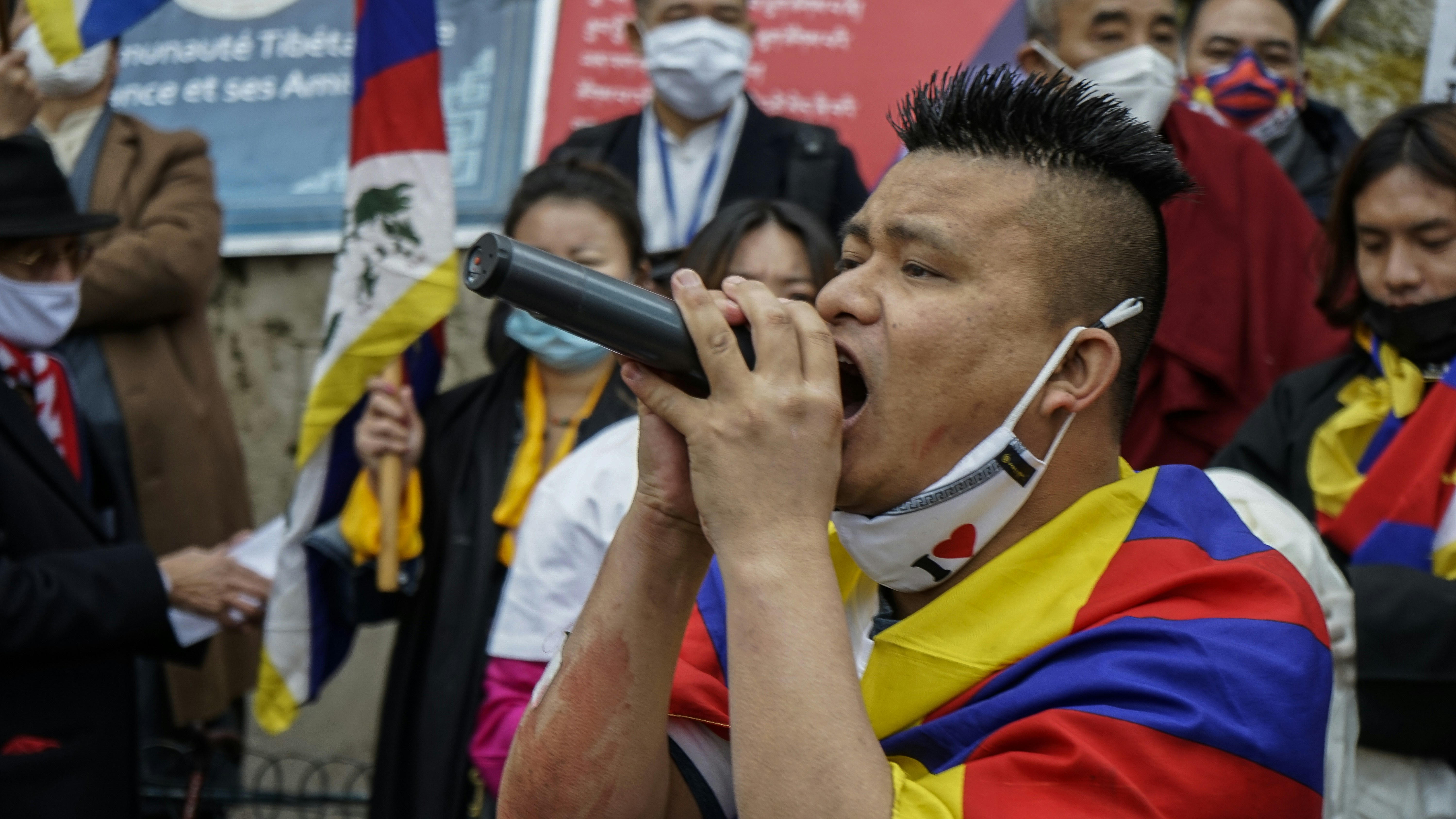 A large crowd of Ladakhi protestors, including men, women, and monks, holding banners with slogans like 