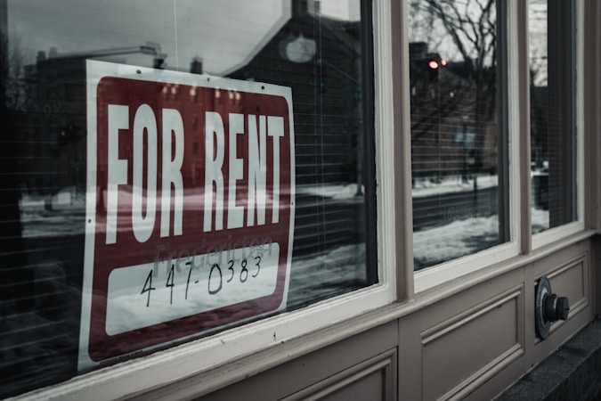 A rental listing sign displayed in a residential window in a neighborhood with available units