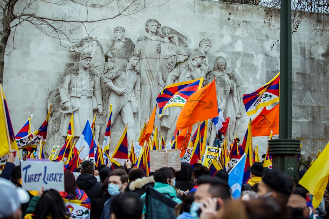 people gathering in front of white concrete wall with flags