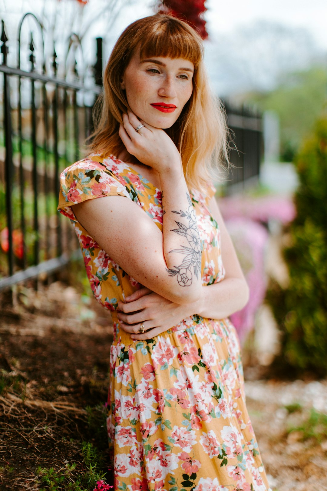 woman in orange and white floral dress standing near fence during daytime