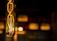 An incandescent light bulb is captured in close-up, with its glowing filament creating a warm, radiant effect. The background is softly blurred, featuring diffused yellow and orange lights that add a sense of depth and ambiance.