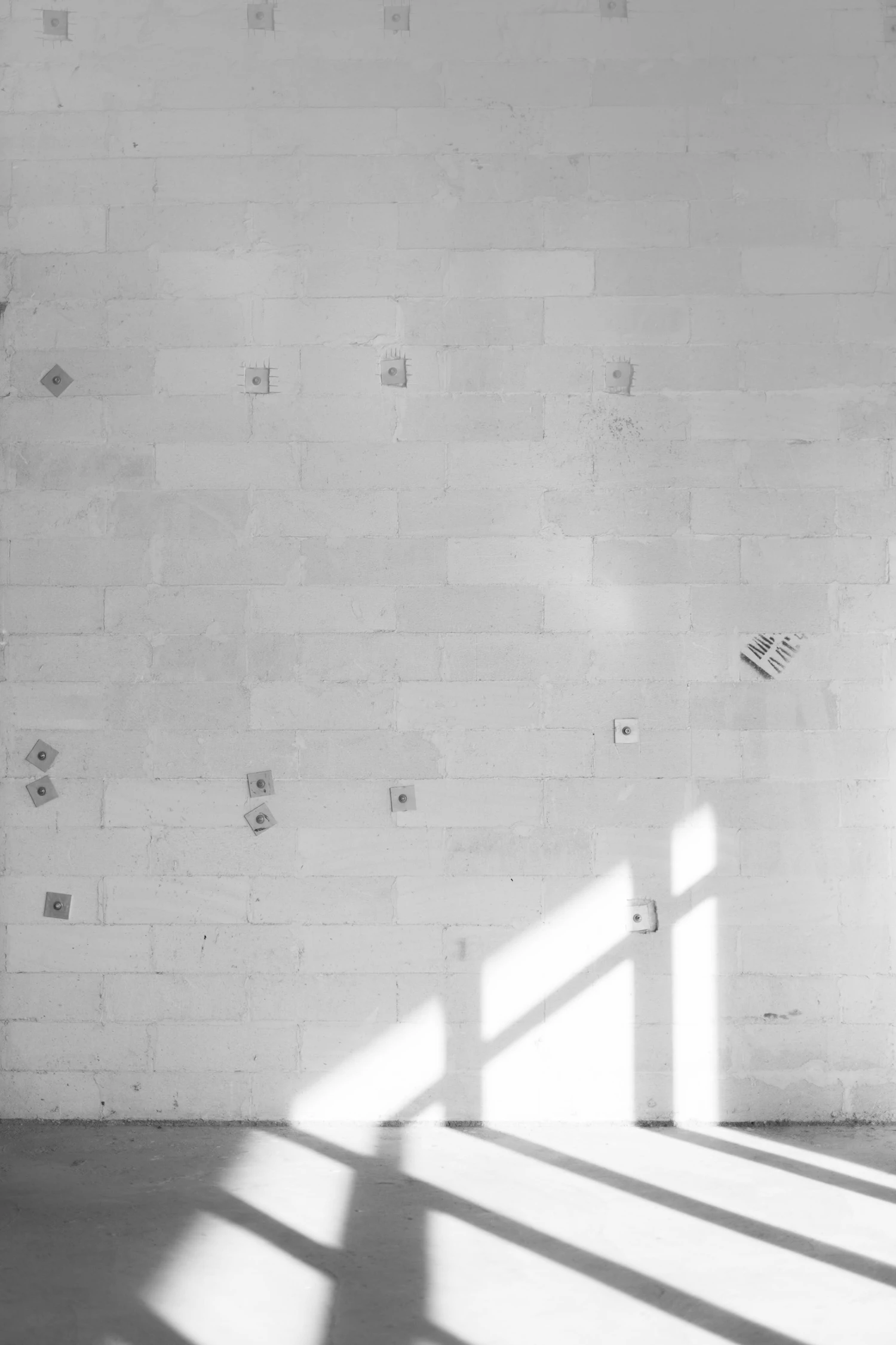 Low sunlight casting window shapes across a pale concrete-block wall and floor