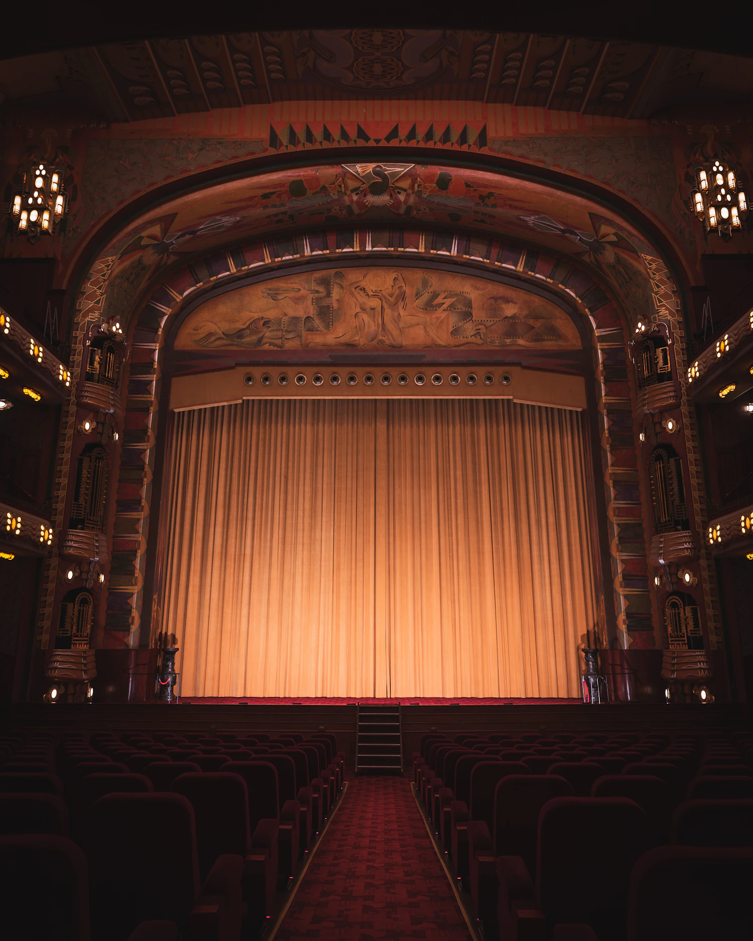 A gilded proscenium stage with a lit golden curtain and rows of red seats
