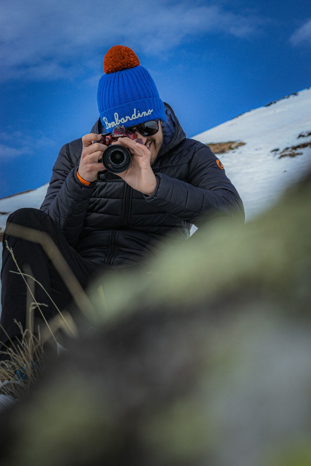 person in black jacket and blue knit cap holding black dslr camera