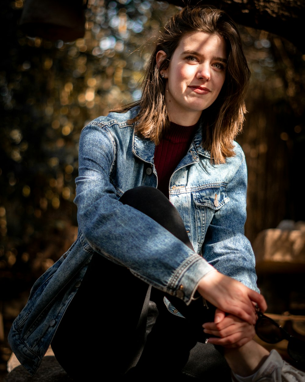 woman in blue denim jacket and black denim jeans sitting on brown wooden bench