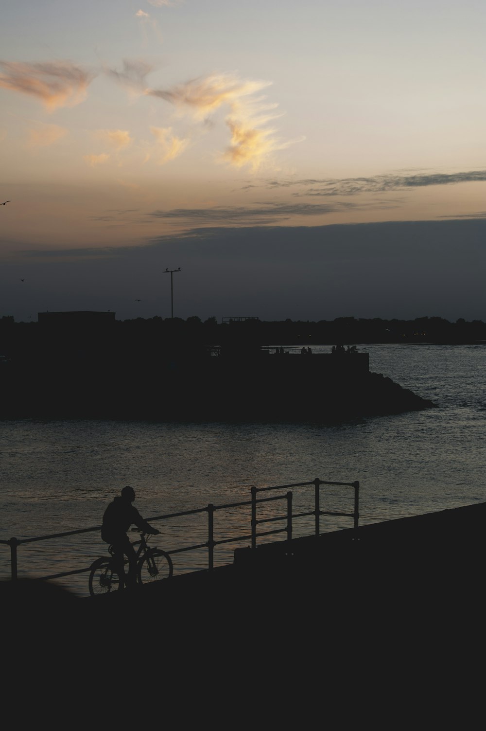 silhouette of man and woman sitting on bench near body of water during sunset