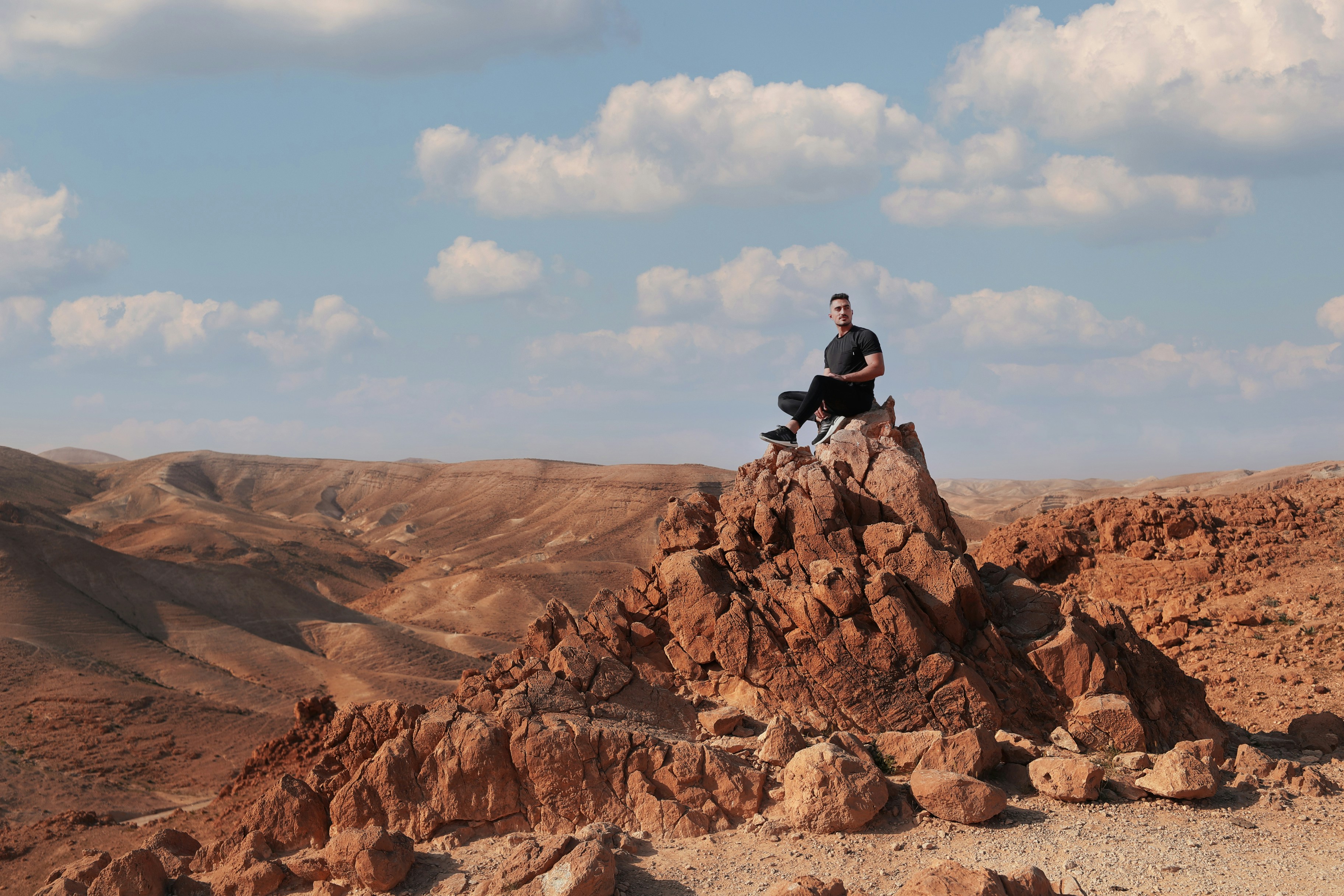 man in black jacket sitting on rock formation during daytime