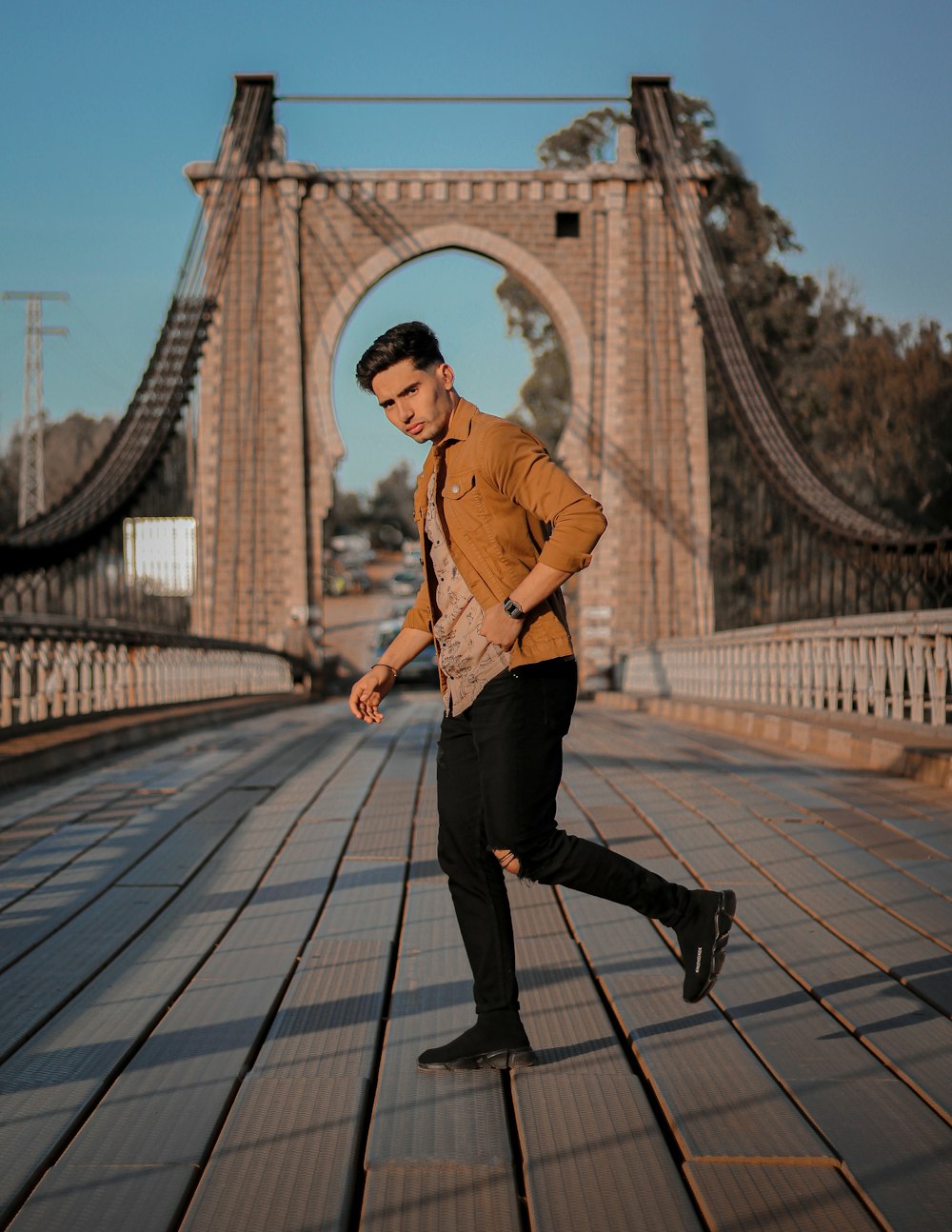 man in brown dress shirt and black pants standing on bridge during daytime