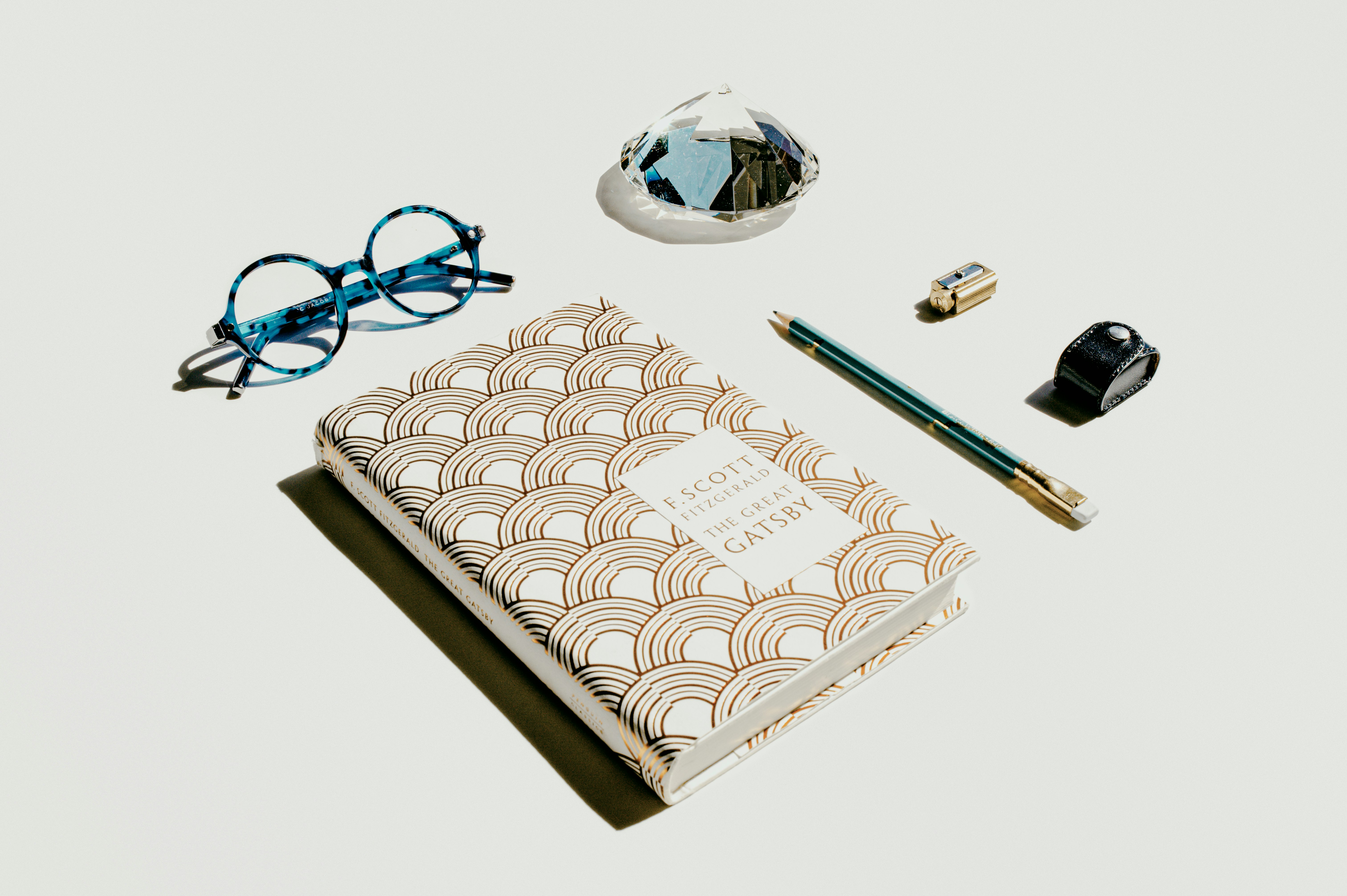 Blue glasses, pencil and sharpener with a copy of The Great Gatsby on white background 