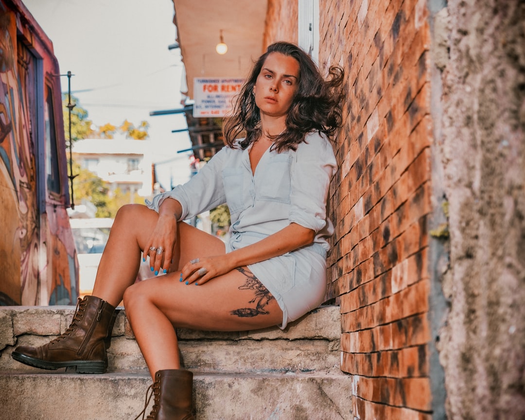woman in white button up shirt and brown shorts sitting on brown brick wall during daytime