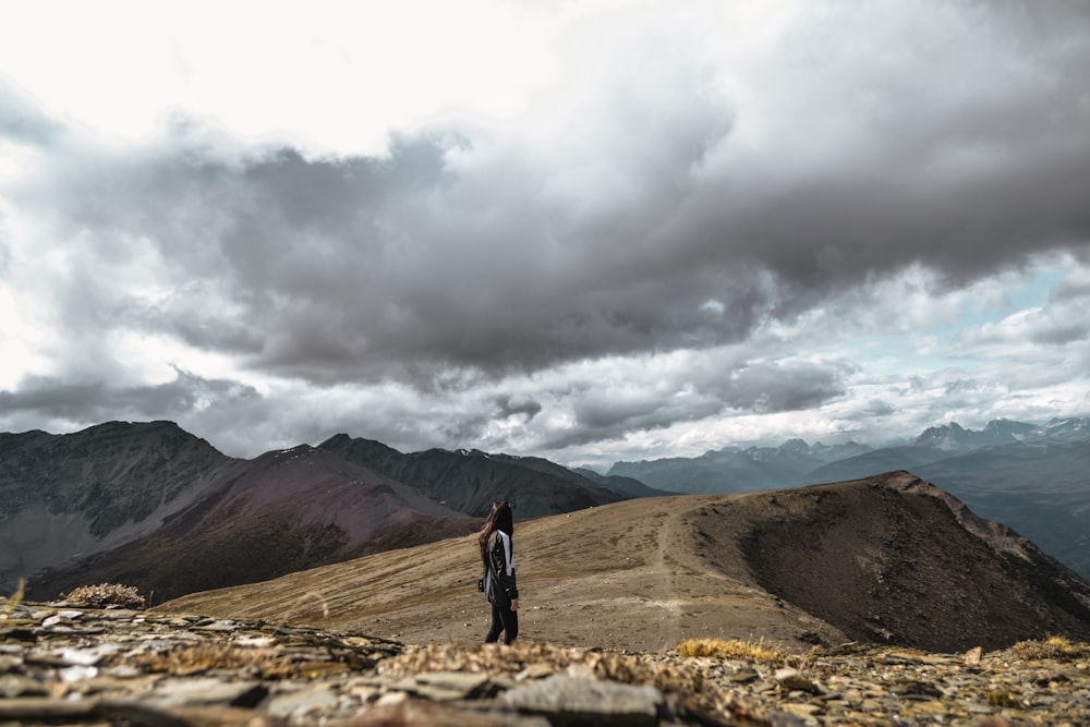 uomo in giacca nera in piedi sulla formazione rocciosa marrone sotto il cielo nuvoloso grigio durante il giorno
