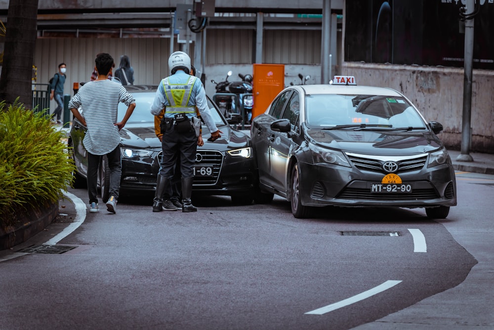 Hombre con camisa de rayas blancas y negras y pantalones negros de pie junto a un coche negro durante el día