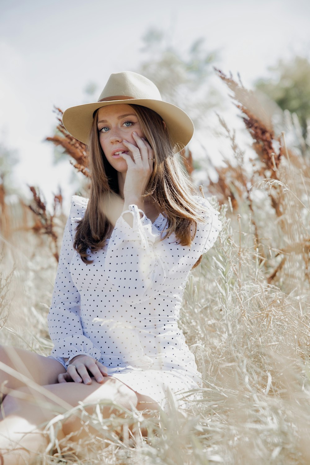 woman in white and blue floral long sleeve shirt and brown hat sitting on brown grass