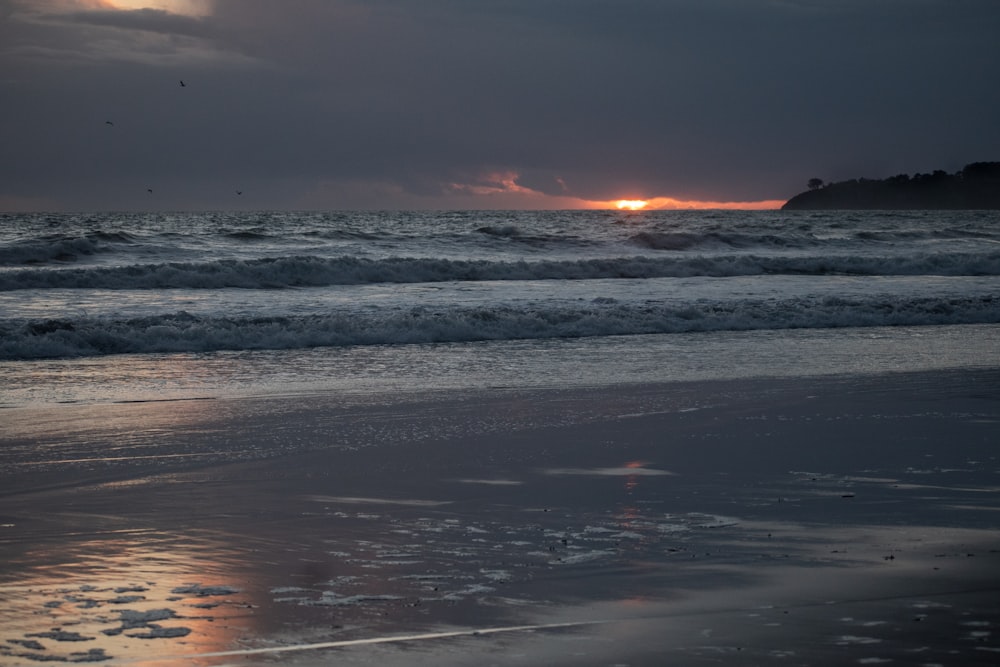 the sun is setting over the ocean on a cloudy day