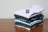 A neatly folded stack of casual wear shirts in different colors on a shelf.