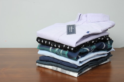 A neatly folded stack of freshly laundered clothes on a wooden table.