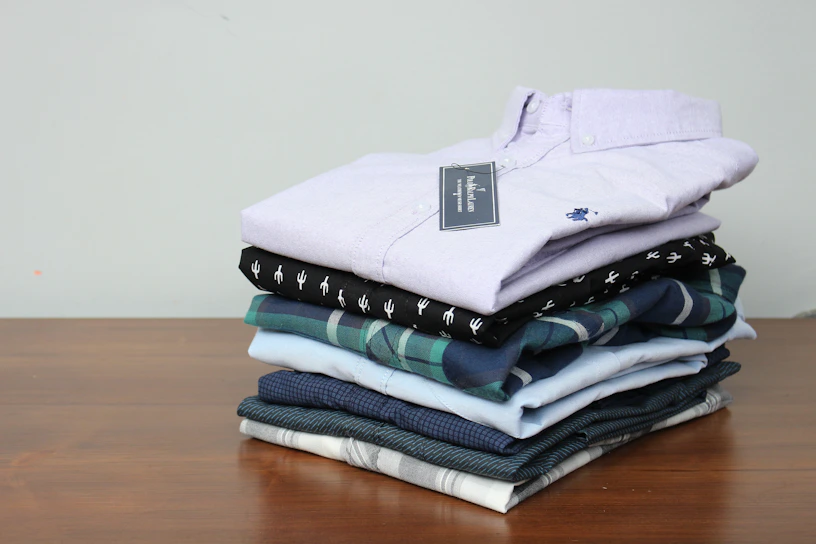 Close-up of fresh, neatly folded blue and white cotton shirts stacked on a clean wooden shelf.