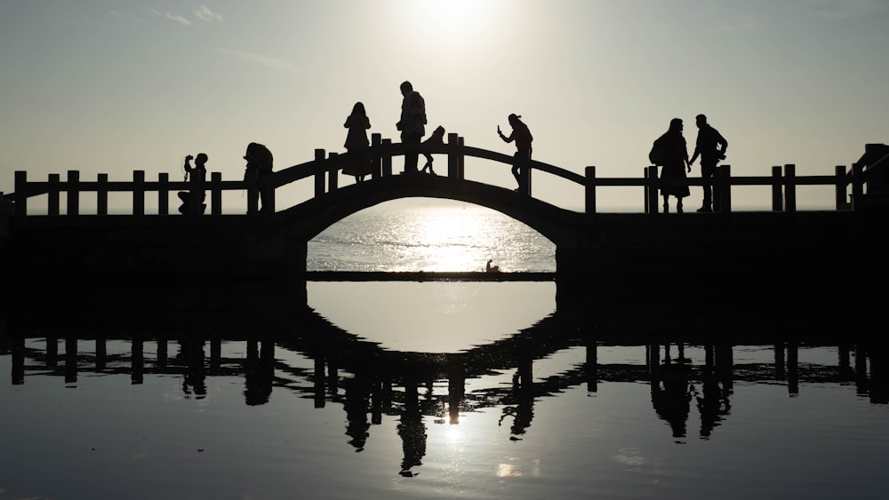 silhouette of people standing on bridge over water during sunset