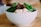 A white bowl filled with noodles, green leafy vegetables, and chunks of braised meat, placed on a wooden surface. The dish includes fresh ingredients that are well-prepared and appetizing.