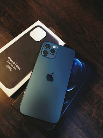 A modern smartphone with a sleek design lies on top of its packaging box, displaying its triple camera setup. The brand logo is prominently visible on the device, and the box also includes branding information.